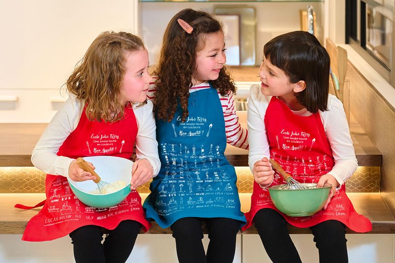 Enfants portant un tablier personnalisé avec dessins d’élèves, idée d’objet pour financer les projets