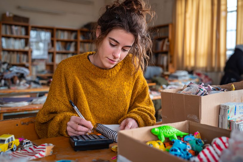 Organisation des lots de kermesse : une bénévole calcule les quantités avec une boîte remplie de jeux