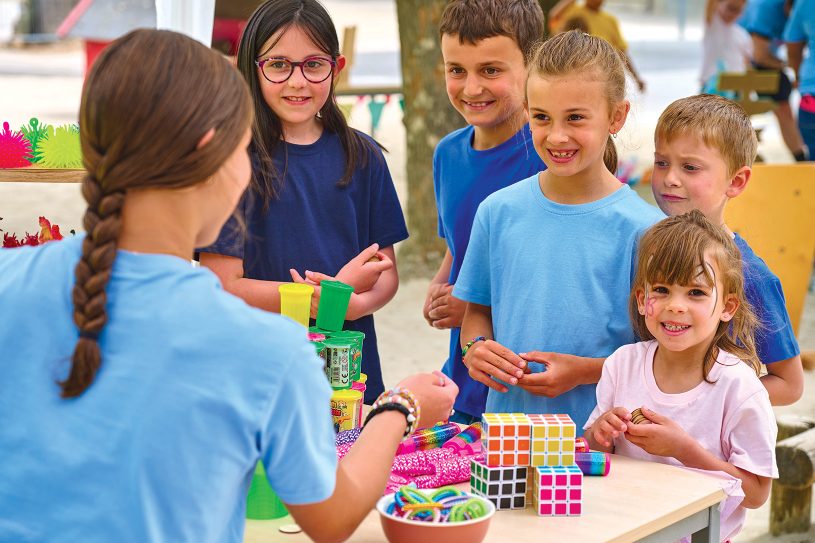 Stand de kermesse animé avec des enfants choisissant leurs lots auprès d’un bénévole.