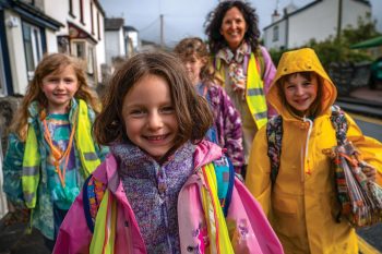 Enfants souriants marchant en groupe vers l’école, accompagnés par un adulte en gilet fluo, illustration du pédibus.